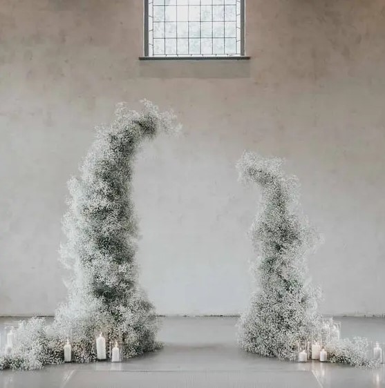 a delicate winter wedding altar compose of white baby's breath and pillar candles catches an eye with its shape