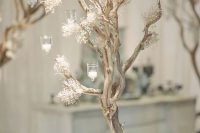 a frozen wedding centerpiece of a tree with blooms and candleholders is a cool idea for a winter wonderland wedding