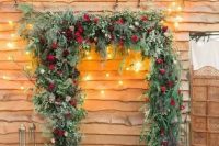 a gorgeous Christmas wedding arch shaped as a frame, covered with evergreens, greenery, red roses and with lots of candle lanterns around