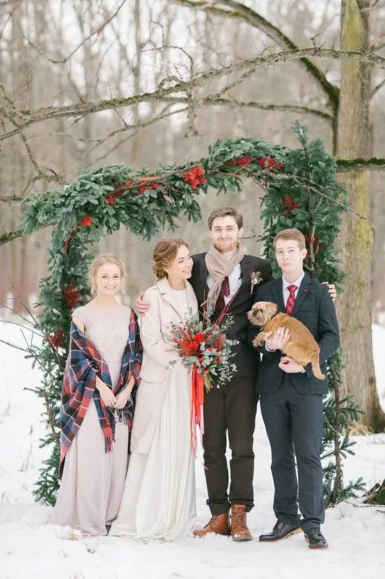 a gorgeous asymmetrical Christmas wedding arch of usual and red spray painted evergreens is a fantastic idea for a snowy holiday wedding