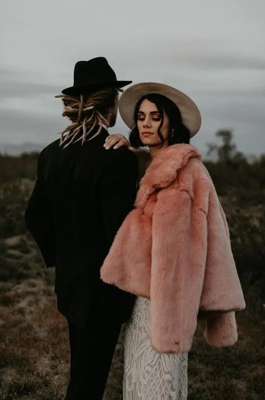 a gorgeous pink faux fur coat over a romantic boho lace wedding dress plus a hat for a boho bridal look