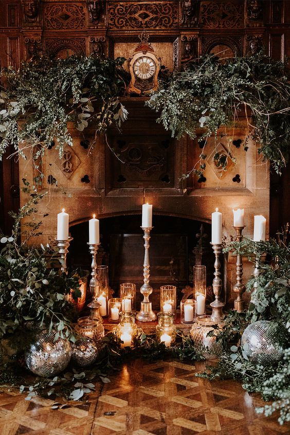 a gorgeous winter wedding backdrop with a fireplace styled with candles and greenery and disco balls is a cool idea for NYE