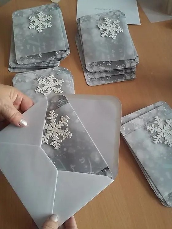 a grey wedding invitation suite with white 3D snowflakes and vellum jackets for them is a chic and lovely idea for a winter wedding