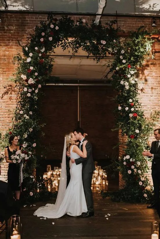 a jaw-dropping Christmas wedding arch covering the doorway, with los of greenery, blush and red blooms and floating candles is amazing