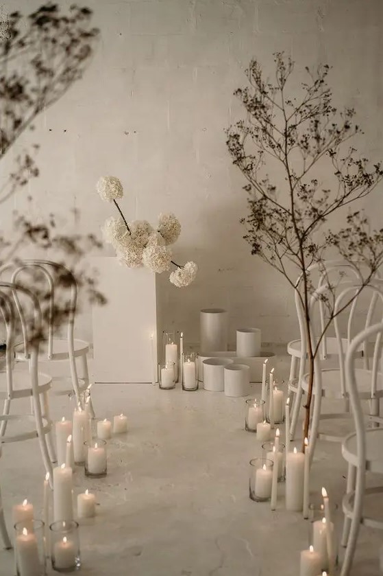 A jaw dropping minimalist winter wedding space with white blooms, vases, dried branches and pillar candles