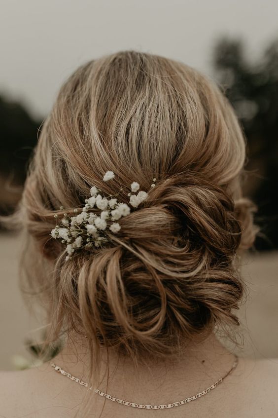 a loose messy low updo with a bump on top and some baby's breath is a cool idea for a bride in any season