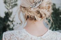 a messy braided low updo with a rhinestone hairpiece plus some locks down is a cool idea for any bride with medium length hair