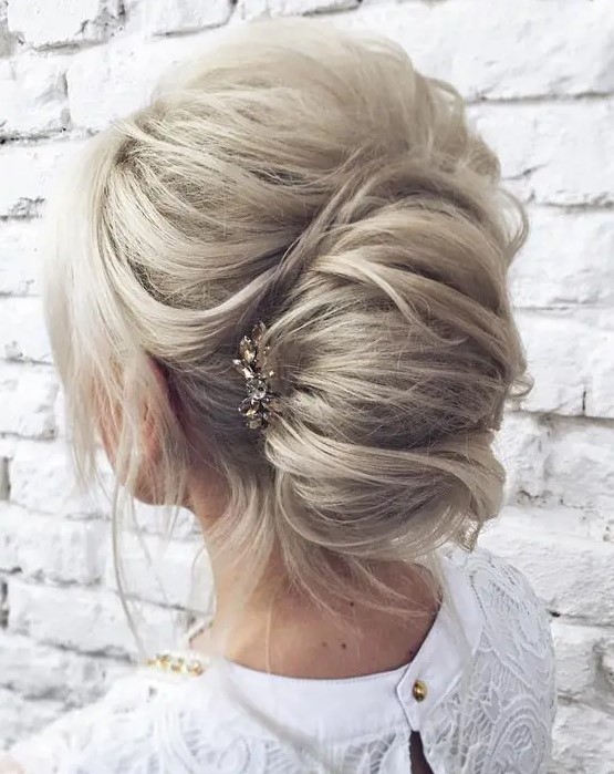a messy casual chignon hairstyle with some waves down and a bump on top plus a rhinestone hairpiece