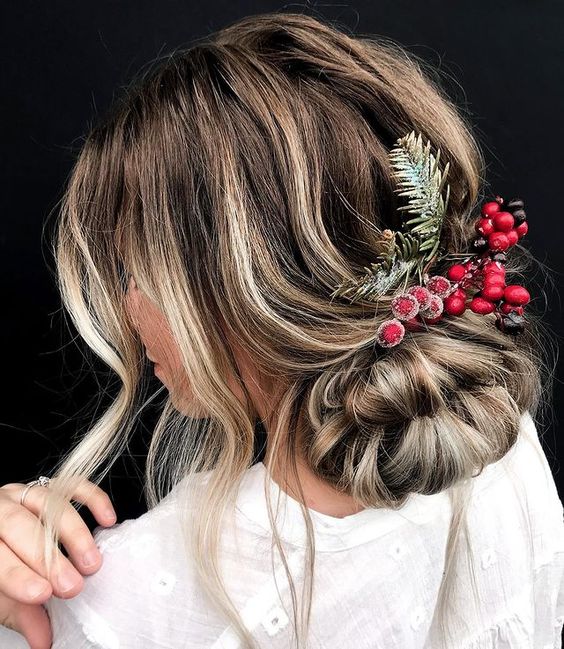 A messy low updo with a bump on top and some face framing hair decorated with evergreens and berries is amazing