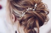 a messy updo with twisted hair a wavy bump on top, some hair down and a rhinestone hairpiece