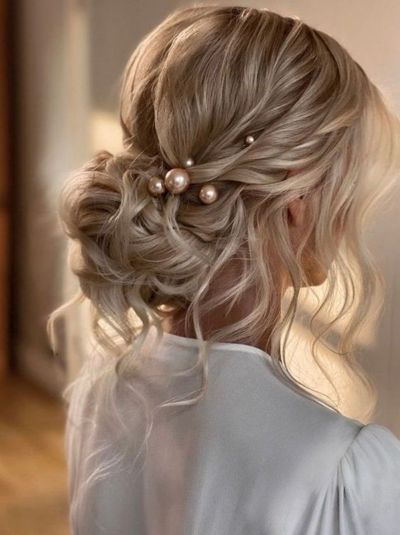 A messy wavy low bun with a wavy top, some locks down and face framing hair plus some large pearl hair pins