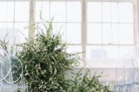 a minimalist winter wedding ceremony space done with greenery and white blooms, pillar candles and clear chairs