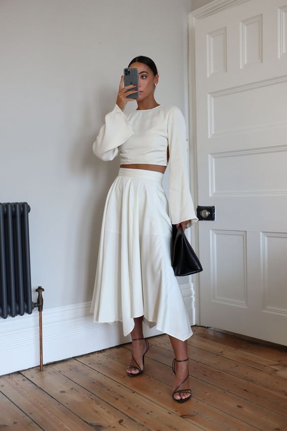 a modern bridal shower look with a pleated midi skirt, a crop top with bell sleeves, black shoes and a black bag