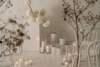a modern white wedding ceremony space with pillar candles, an altar, branches and white chairs is stylish and cool