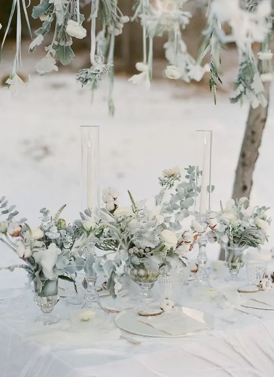 a neutral winter wedding tablescape styled with pale greenery and white blooms and the same over the table, neutral plates and menus