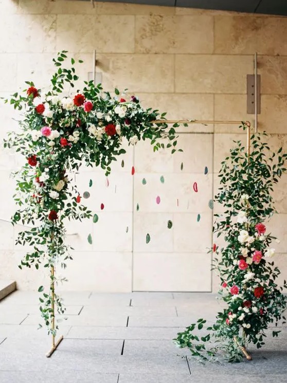a red and green wedding arch with greenery, blooms and hanging agates for a trendy feel