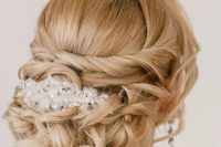 a refined formal twisted and curled updo with a bump, some locks framing the face and a large rhinestone hairpiece