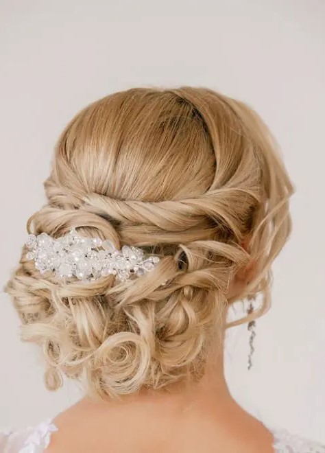 a refined formal twisted and curled updo with a bump, some locks framing the face and a large rhinestone hairpiece