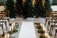 a row of Christmas trees with no decor at all for a natural feel, greenery and magnolia leaves plus candles to line up the aisle