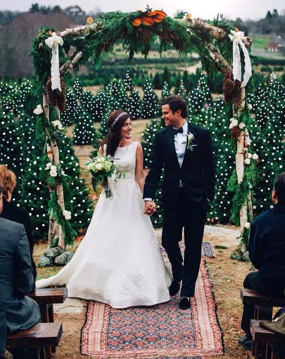a rustic winter wedding arch with evergreens, white blooms, leaves and oversized pinecones is a cool idea for a Christmas wedding