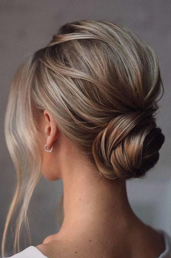 a simple twisted and wrapped low bun with a bump on top and some face-framing locks is a cool idea for a modern and glam bride