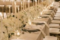 a sophisticated white winter wedding tablescape with lush wite florals and tall and thin candles is very chic and beautiful