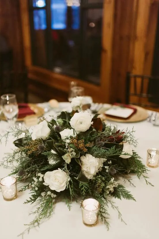 A stylish and non typical Christmas wedding centerpiece of greenery ferns, white blooms and magnolia leaves is pure beauty