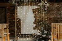 a wedding backdrop with lights and lush florals and greenery creates a romantic and welcoming ambience in the ceremony space