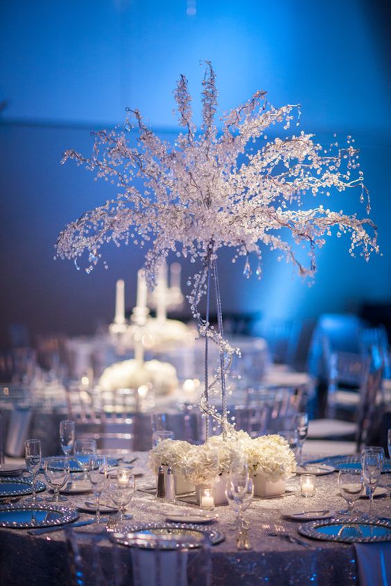 a white and silver winter wonderland wedding table with crystals and white blooms plus candles, silver chargers