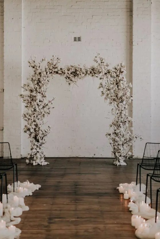 a white cotton wedding arch and pillar candles lining up the aisle are a cool combo for a winter wedding