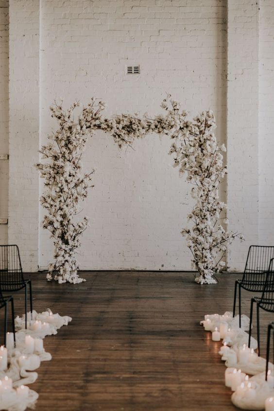 a white cotton wedding arch and pillar candles lining up the aisle are a cool combo for a winter wedding