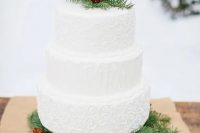a white textural wedding cake displayed on fir branches and decorated with them