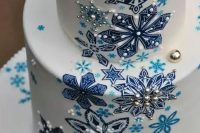 a white wedding cake with painted blue and navy snowflakes, with sugar patterns and edible beads and pearls is amazing for a winter wedidng