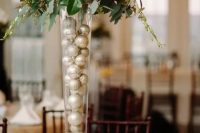 a winter wedding centerpiece of a tall vase filled with ornaments, greenery, twigs and white blooms is ideal for a winter wedding