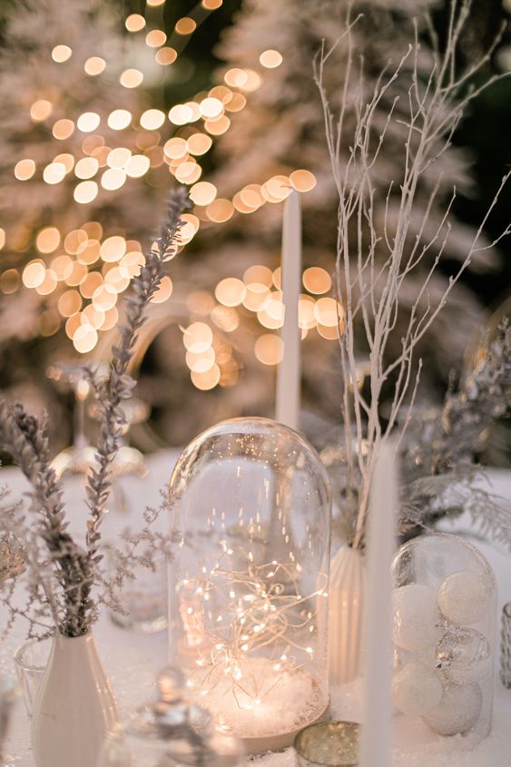 a winter wonderland wedding centerpiece with a cloche with lights, ornaments, frozen branches and tall and thin candles