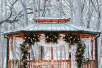 a winter wonderland wedding ceremony space with a gazebo and greenery and white blooms forming an arch