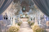 a winter wonderland wedding ceremony space with greenery and white blooms, frozen trees with ornaments and white chairs