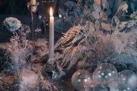 a winter wonderland wedding table with candles, a white dried flower and leaf centerpiece, clear plates and clear ornaments