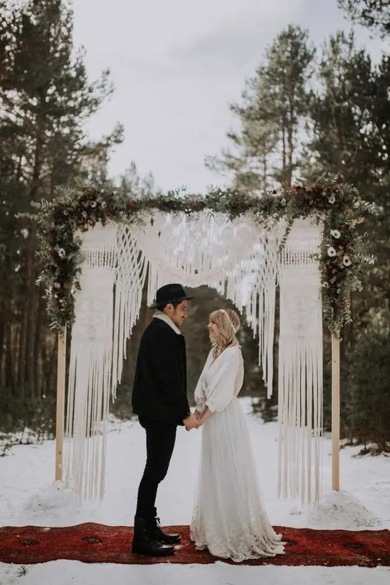 a woodland boho wedding arch with macrame, greenery and white blooms is a lovely idea for a winterwedding