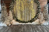 an adorable winter wonderland wedding ceremony space with a round light wedding arch and silver flocked Christmas trees