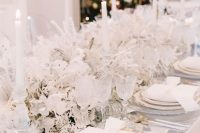 an exquisite white winter wonderland wedding tablescape with frozen blooms and leaves, tall and thin candles and gold touches