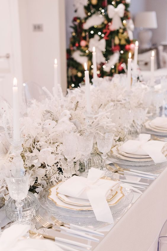 an exquisite white winter wonderland wedding tablescape with frozen blooms and leaves, tall and thin candles and gold touches