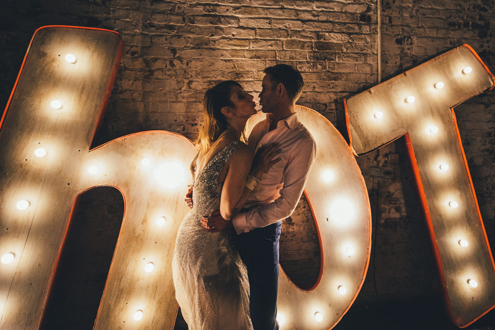 This photo of a beautiful couple in front of an oversized marquee light is hot and sums up the whole wedding