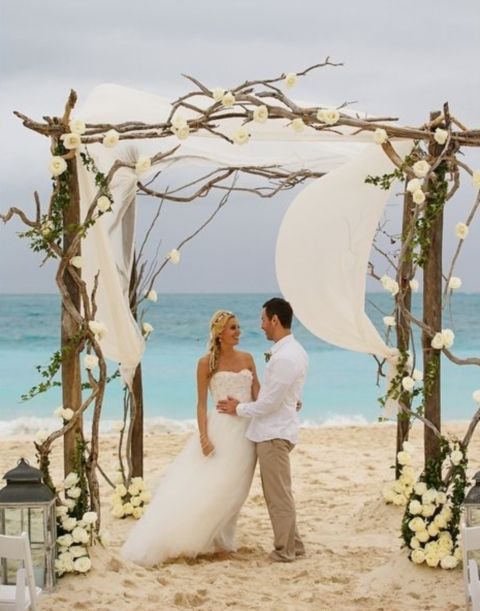 driftwood wedding arch decorated with white fabric and flowers for a beach wedding