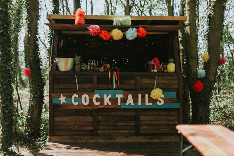 A cute rustic cocktail bar was decorated with colorful pompoms and paper, there was a marquee light