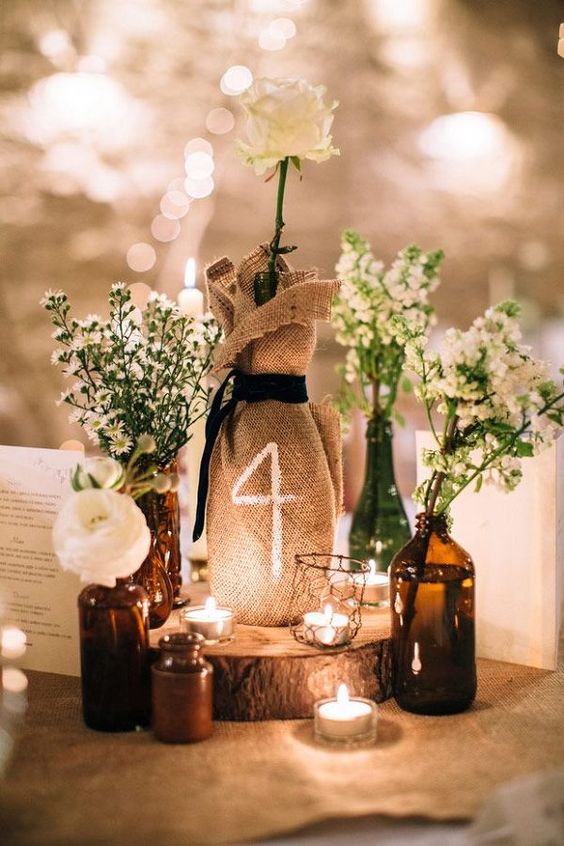 centerpiece with small bottles with flowers and tealights, table number on the burlap sack