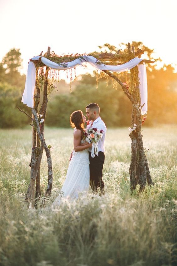 rough tree branches arch topped with white fabric and greenery