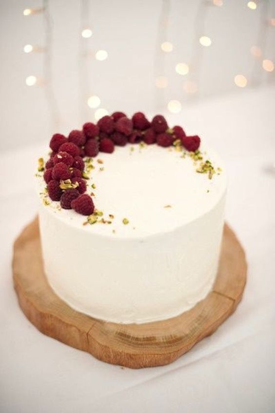 one-tier wedding cake topped with raspberries and pistachios