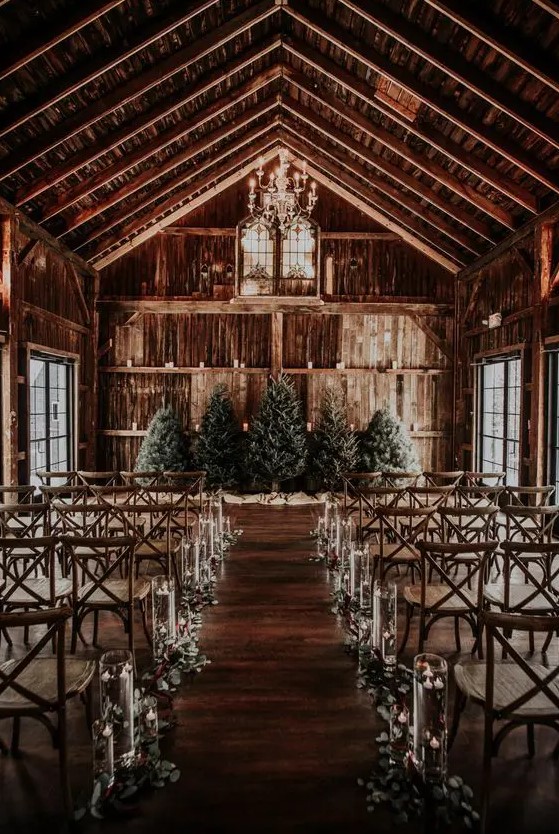 a barn wedding ceremony space with Christmas trees, floating candles adn greenery is a perfect place to tie the knot