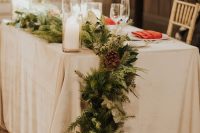 a beautiful and lush Christmas table runner of evergreens, pinecones and pillar candles is a cool idea